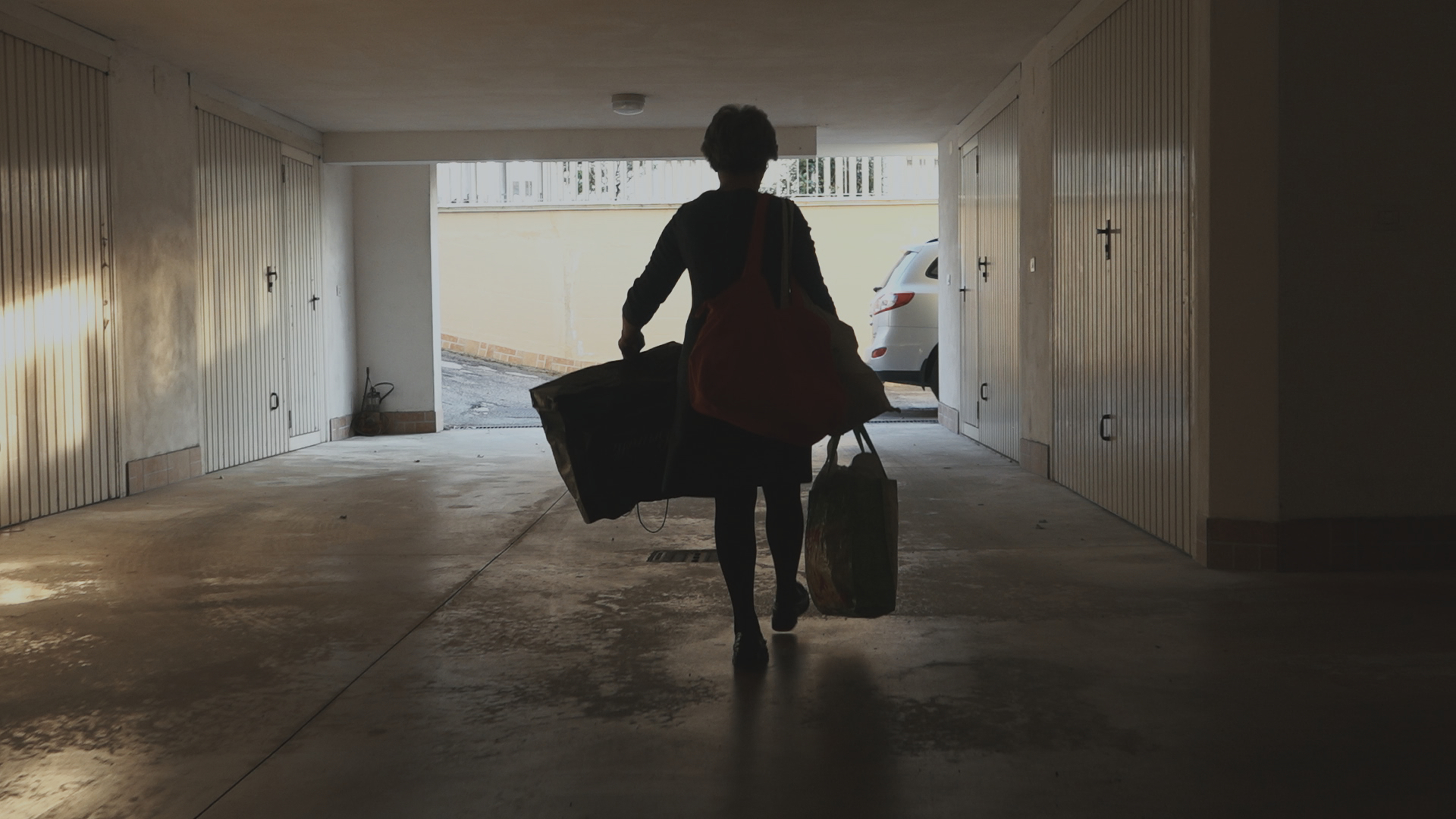 Filmstill aus "Una Primavera": Die Hauptprotagonistin ist von hinten sichtbar, wie sie mit gepackten Koffern durch eine Unterführung geht